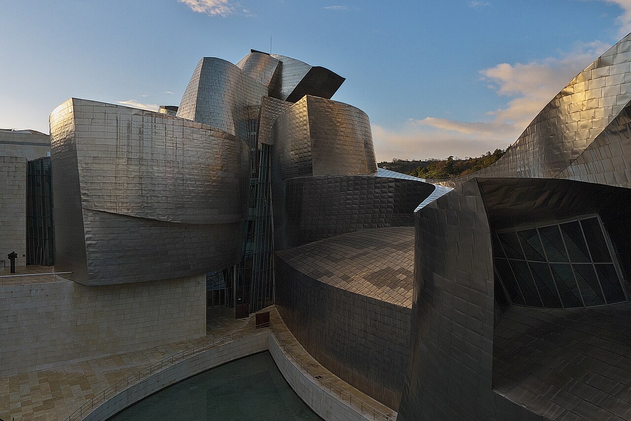 Titanium curves of the Guggenheim Museum Bilbao beside the river, with the city and hills behind