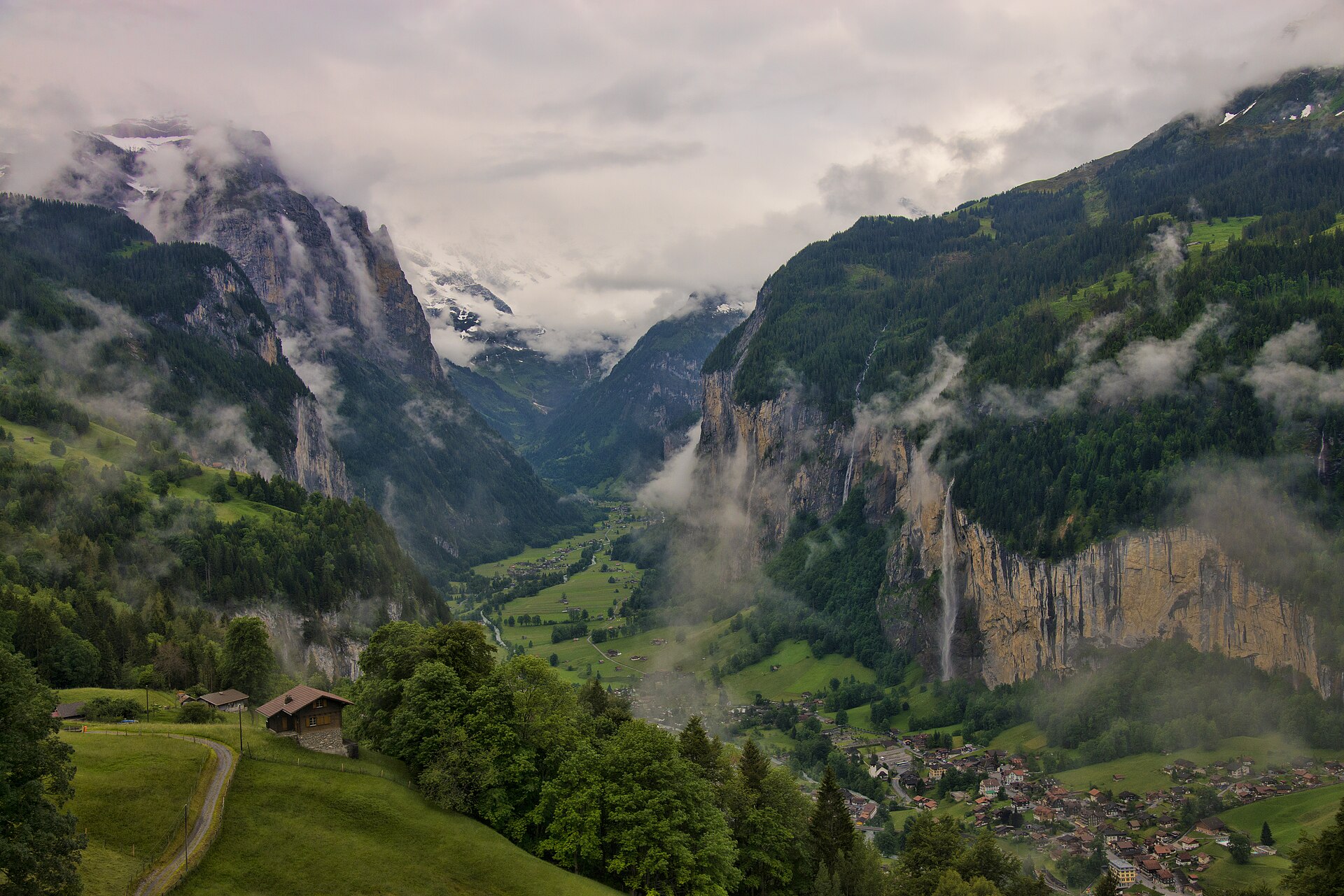 The Lauterbrunnen valley seen from above Wengen, with Staubbach Falls dropping over the cliff on the right, the village on the valley floor and cloud on the peaks at the head of the valley