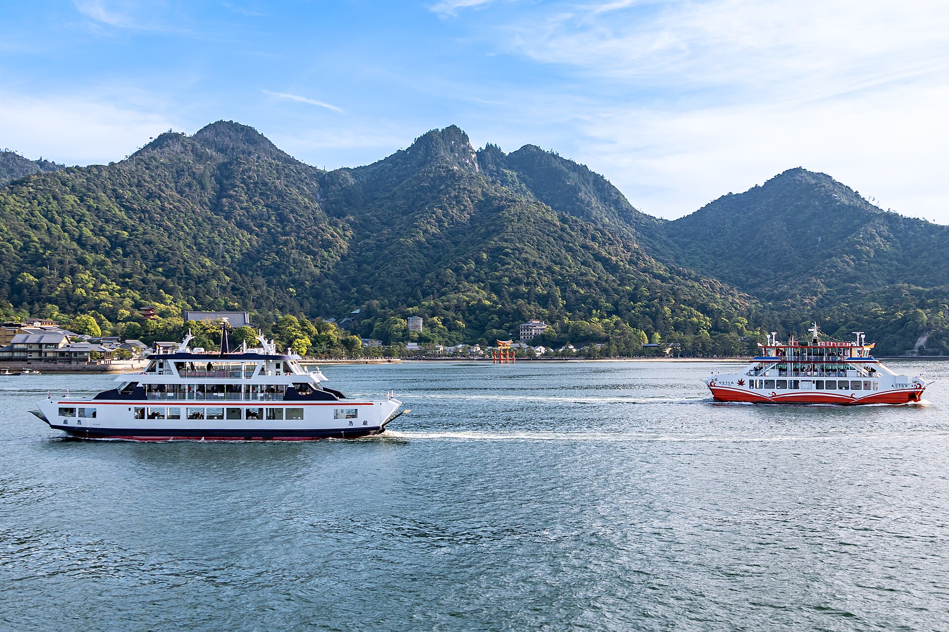 Two Miyajima ferries crossing in front of Itsukushima, with Mount Misen behind and the Great Torii small at the shoreline