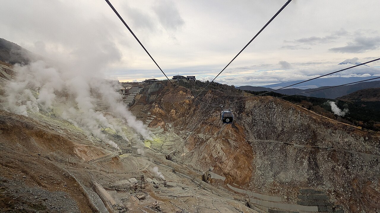 A Hakone Ropeway gondola crossing Owakudani’s steaming volcanic valley, with mountains and a distant snow-capped peak beyond