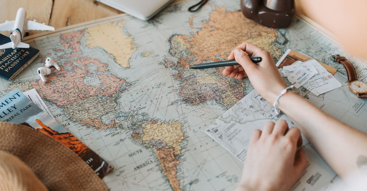 Hands marking destinations on a world map with travel essentials